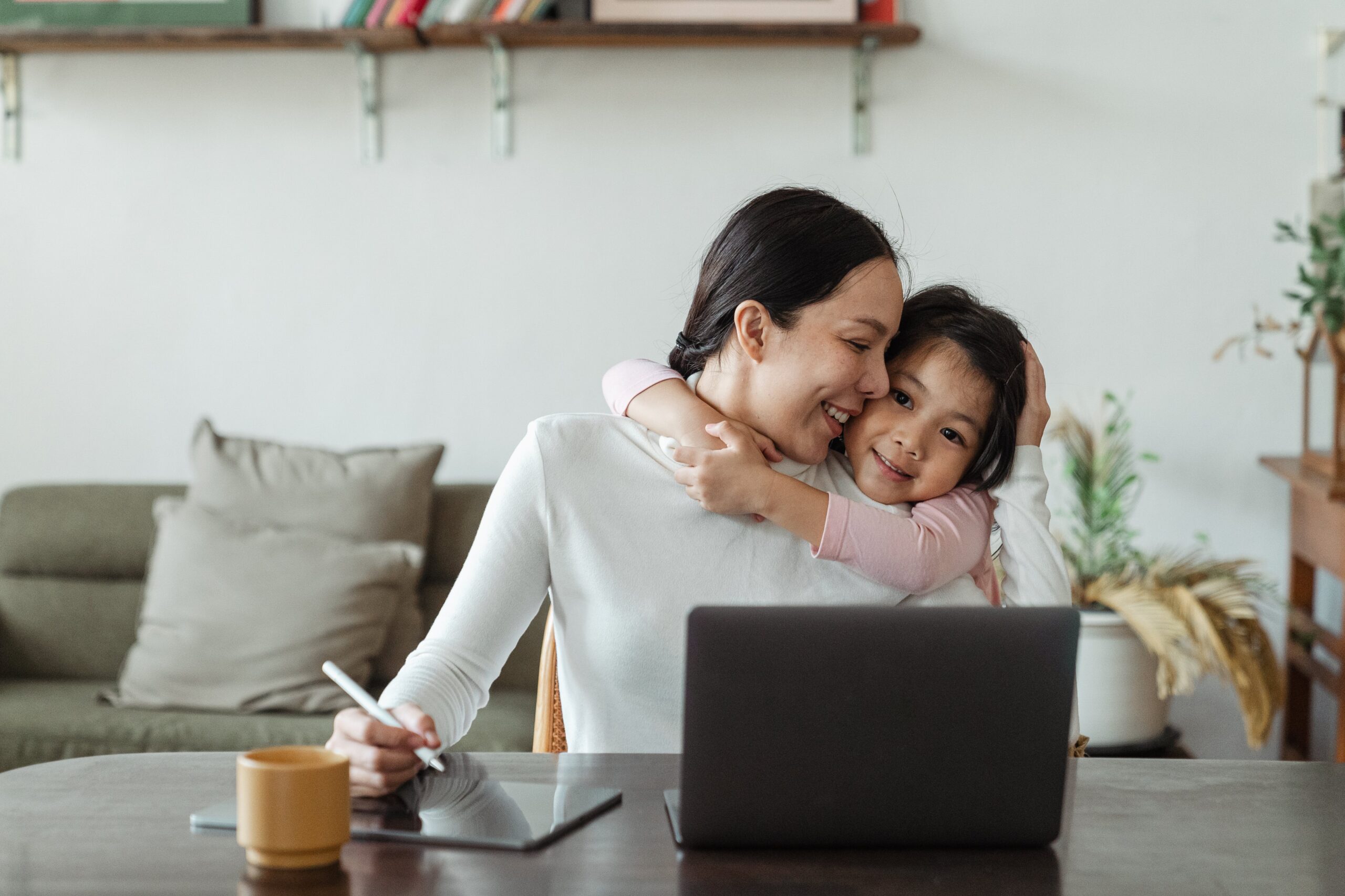 A smiling woman working from home with daughter, demonstrating employee wellbeing 